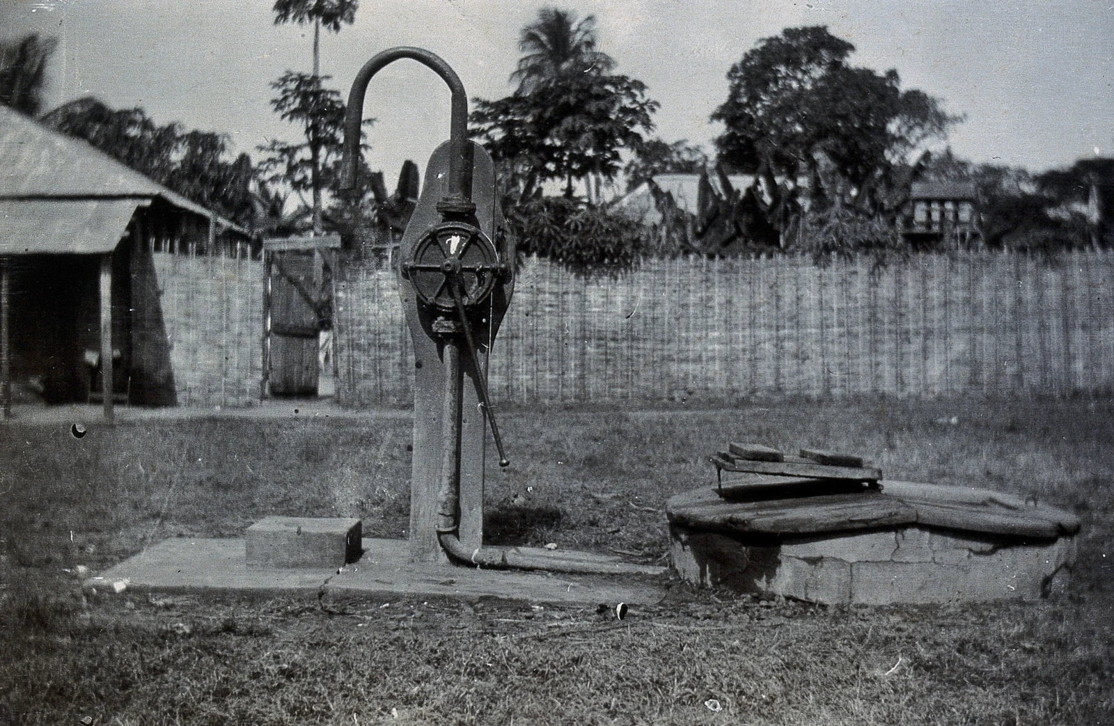 Black-and-white photograph of a hand pump and low well platform beside woven fencing in Bathurst.